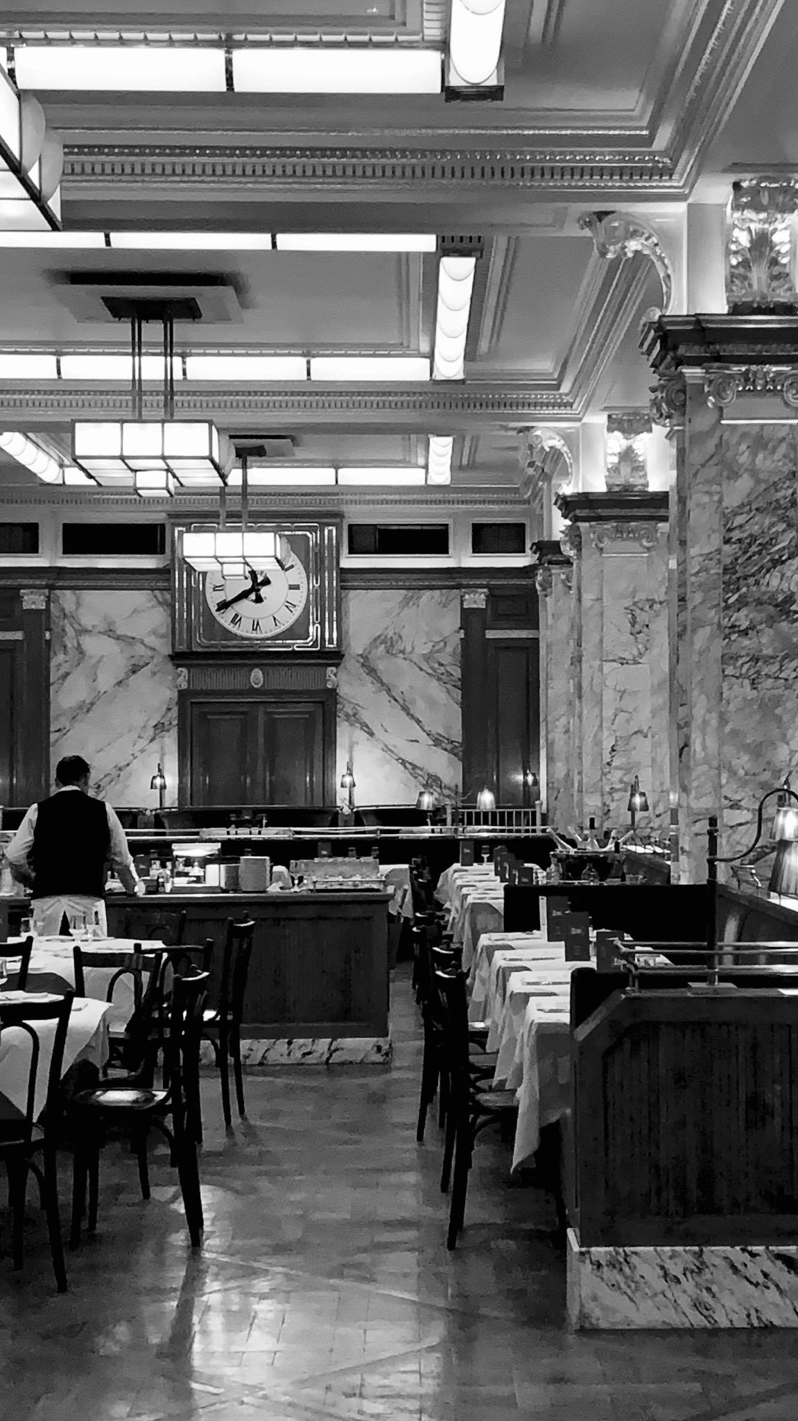 Black and white photograph of a grand dining interior with marble and a central clock