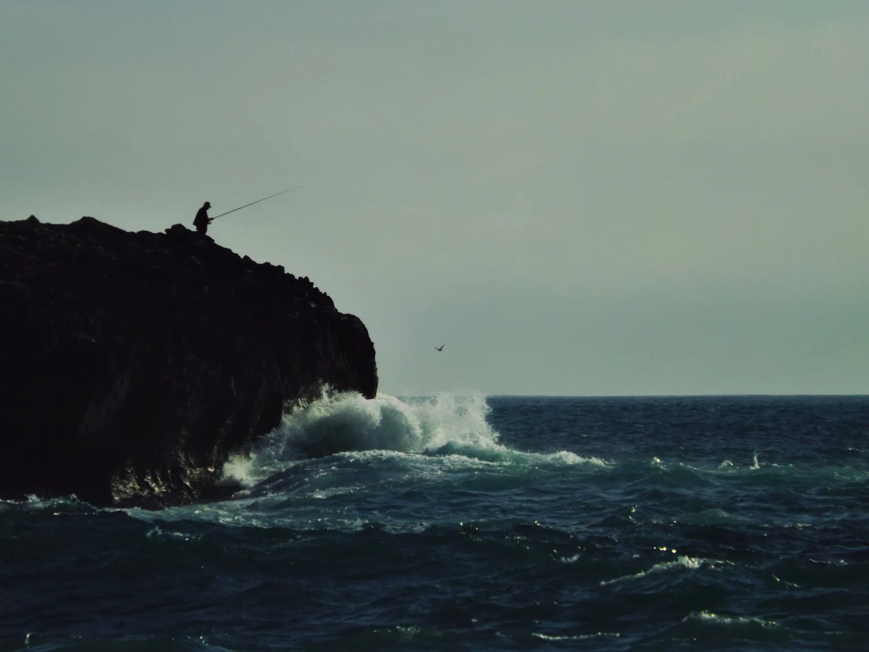 Fisherman on rocks in a vintage-toned photograph